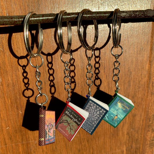 4 mini book keychains hanging from a stick