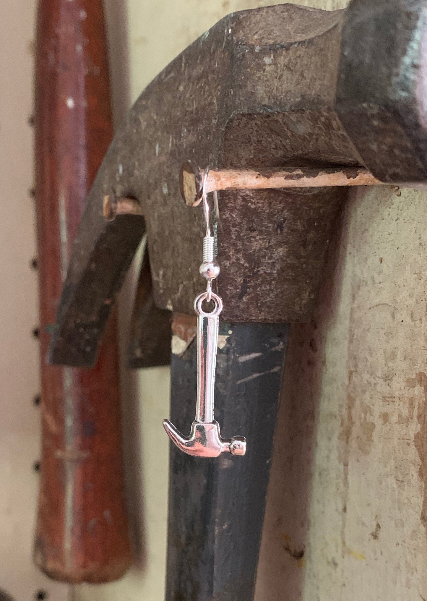 hammer earring hanging on a nail in front of an actual hammer