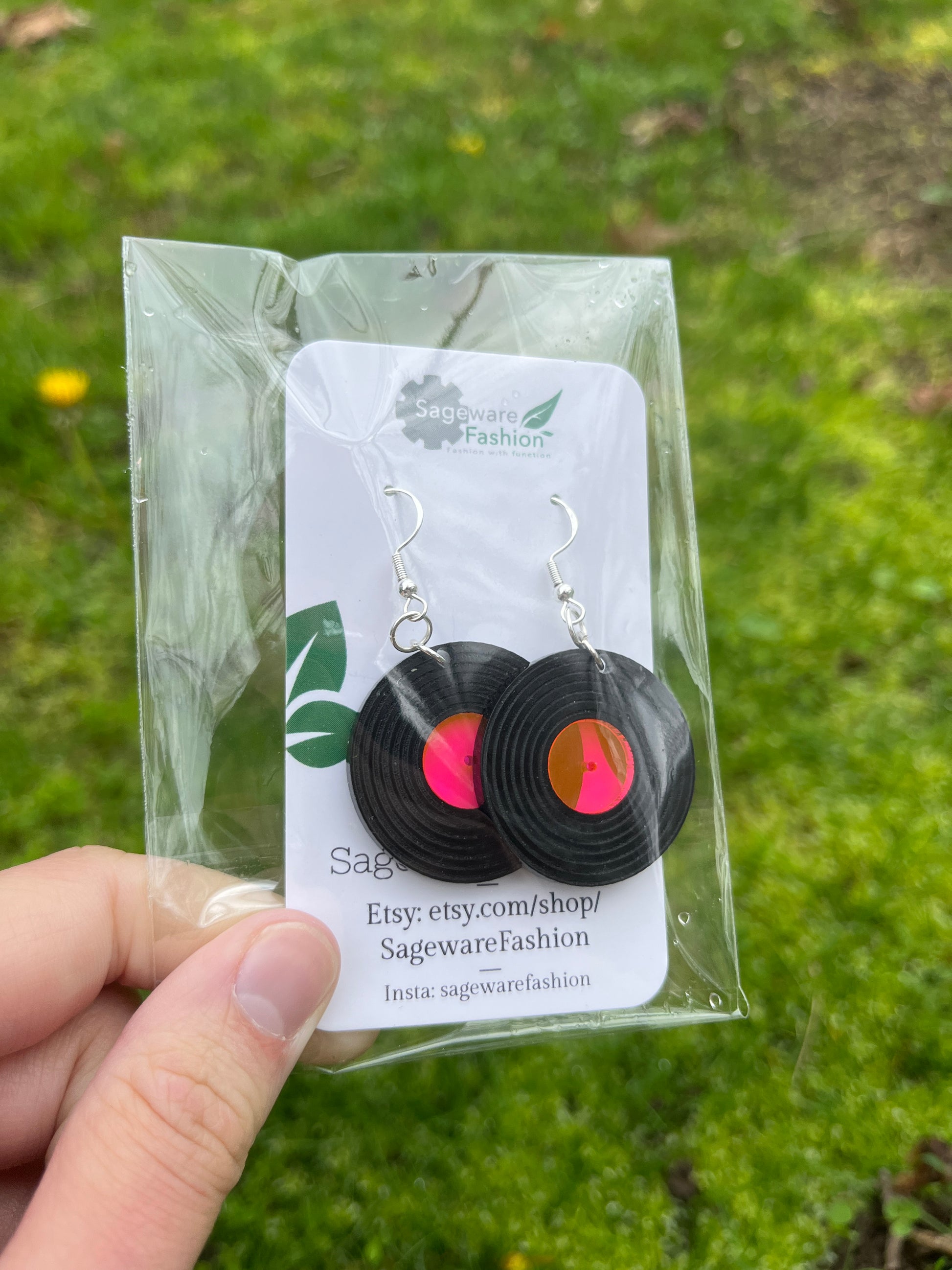 record earrings in packaging being held over grass background
